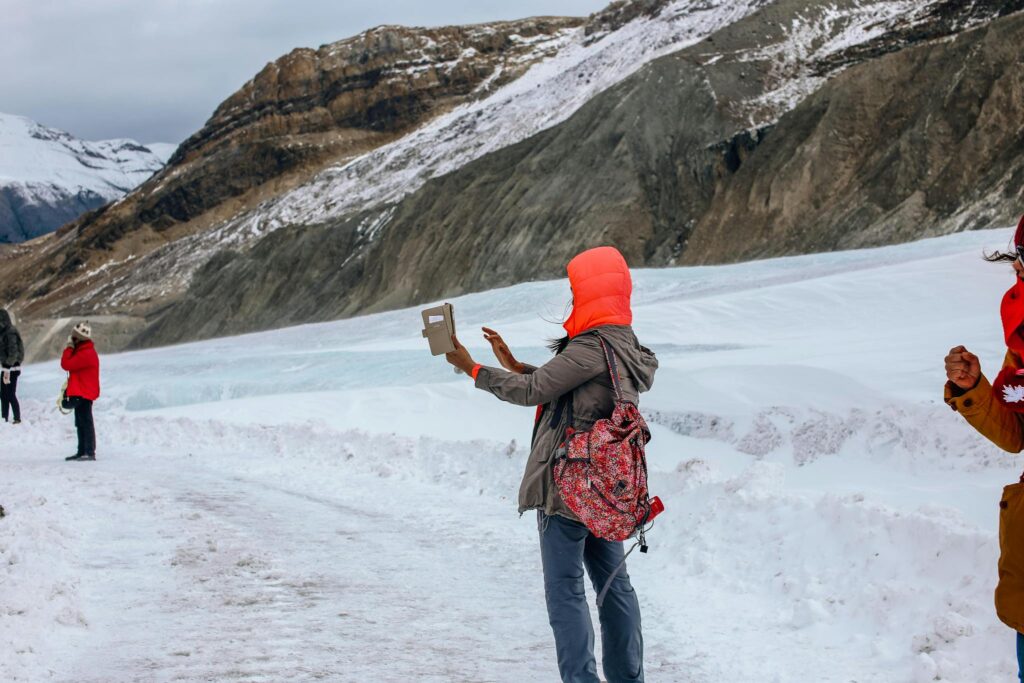 Group of adults hiking in snowy mountainous landscape, capturing moments with camera and tablet.